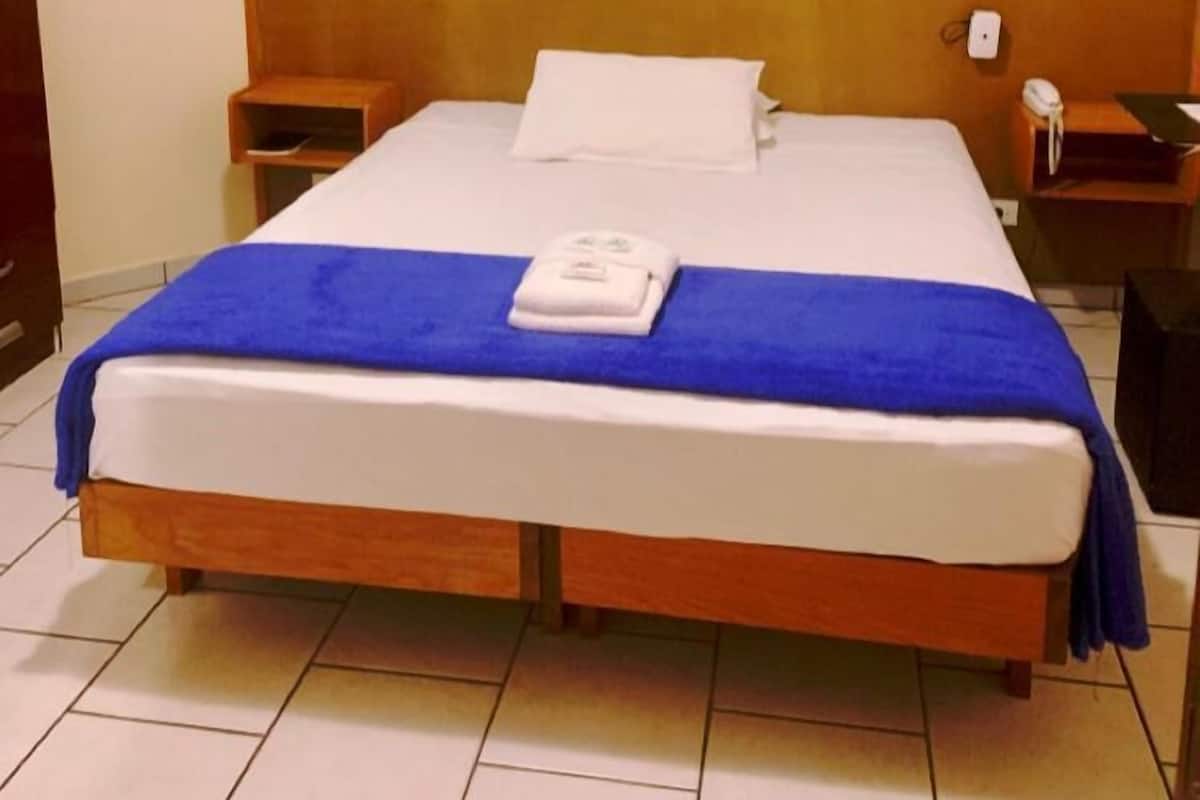 A hotel room with a large bed, a wooden headboard, a nightstand with a phone, and a framed picture on the wall.