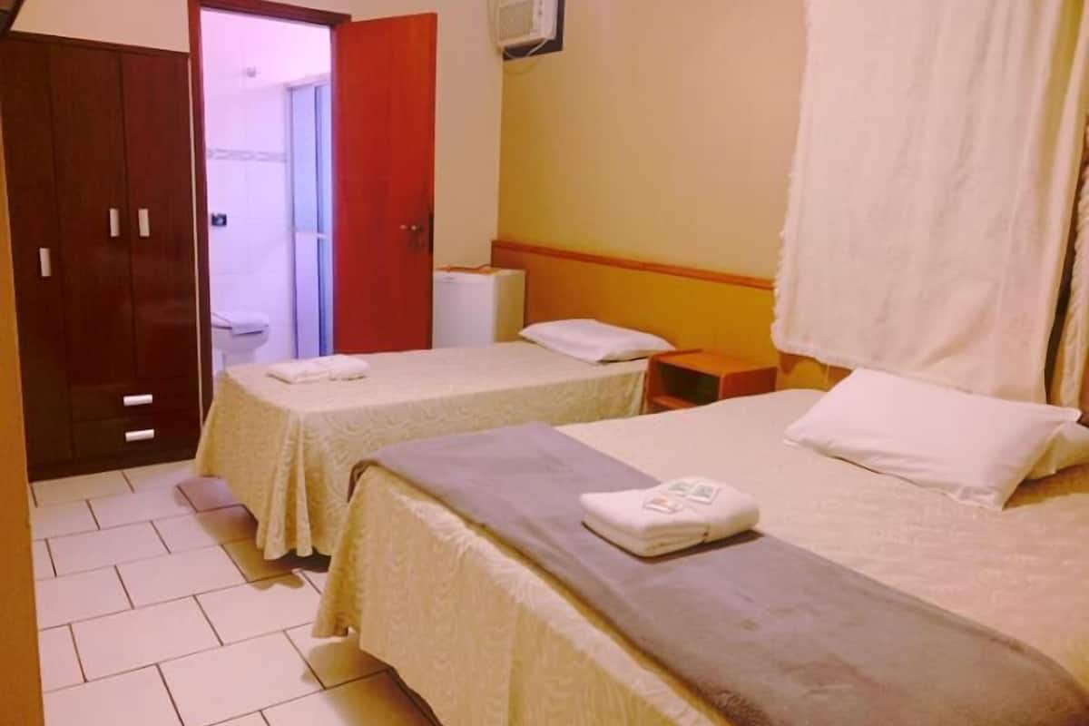 A hotel room with two beds, a wardrobe, and a bathroom visible through an open door.