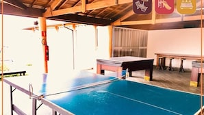 A ping pong table in a covered area with a pool table and chairs in the background. - Hotel Imigrantes LTDA (São Pedro)