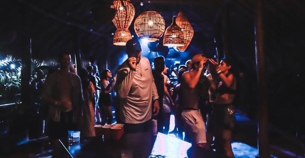 Un espace intérieur bondé, rempli de monde, peut-être une discothèque ou un bar, avec des lumières suspendues et des tables.