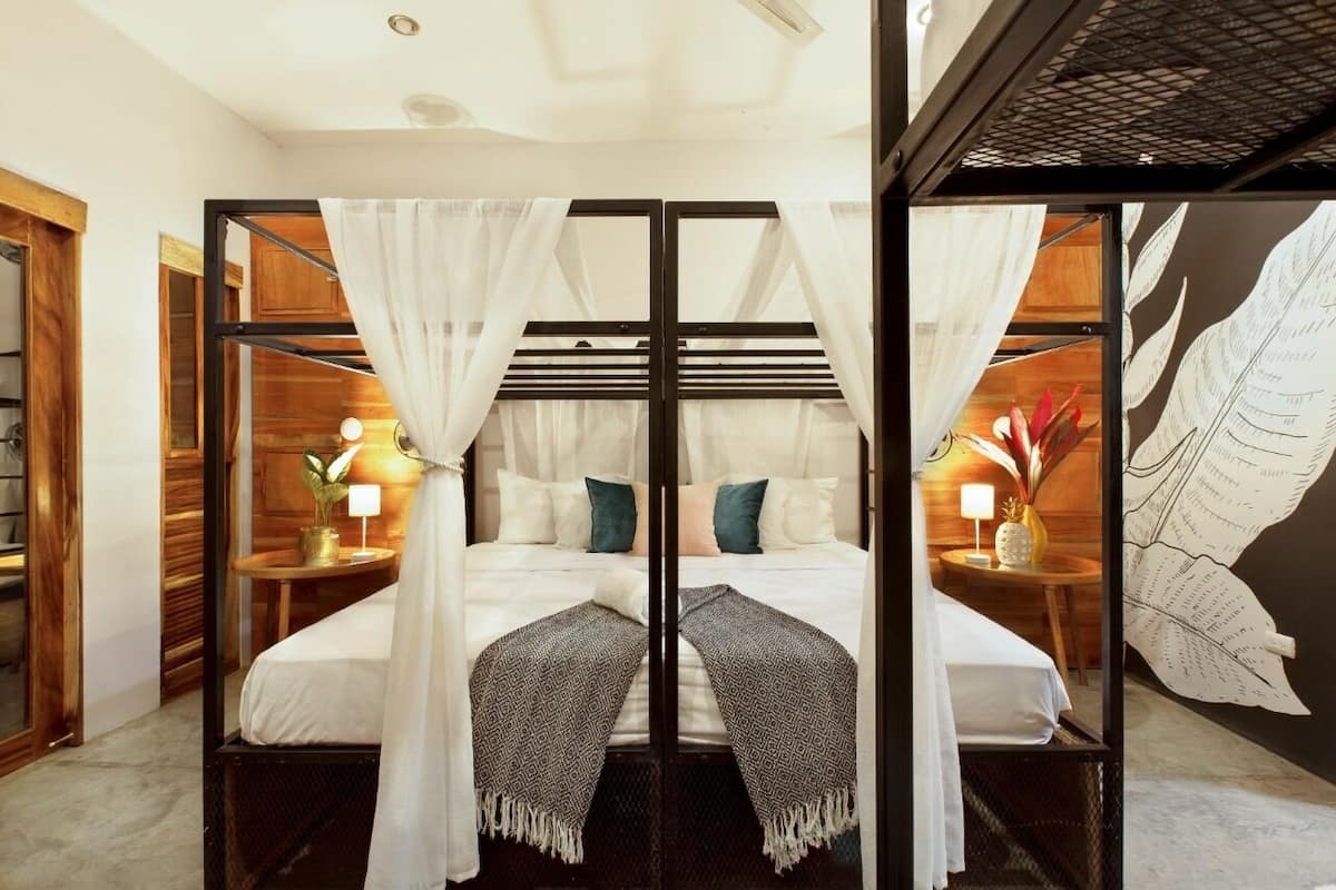 A room with a bed, two bedside tables, and a wall with a leaf pattern.