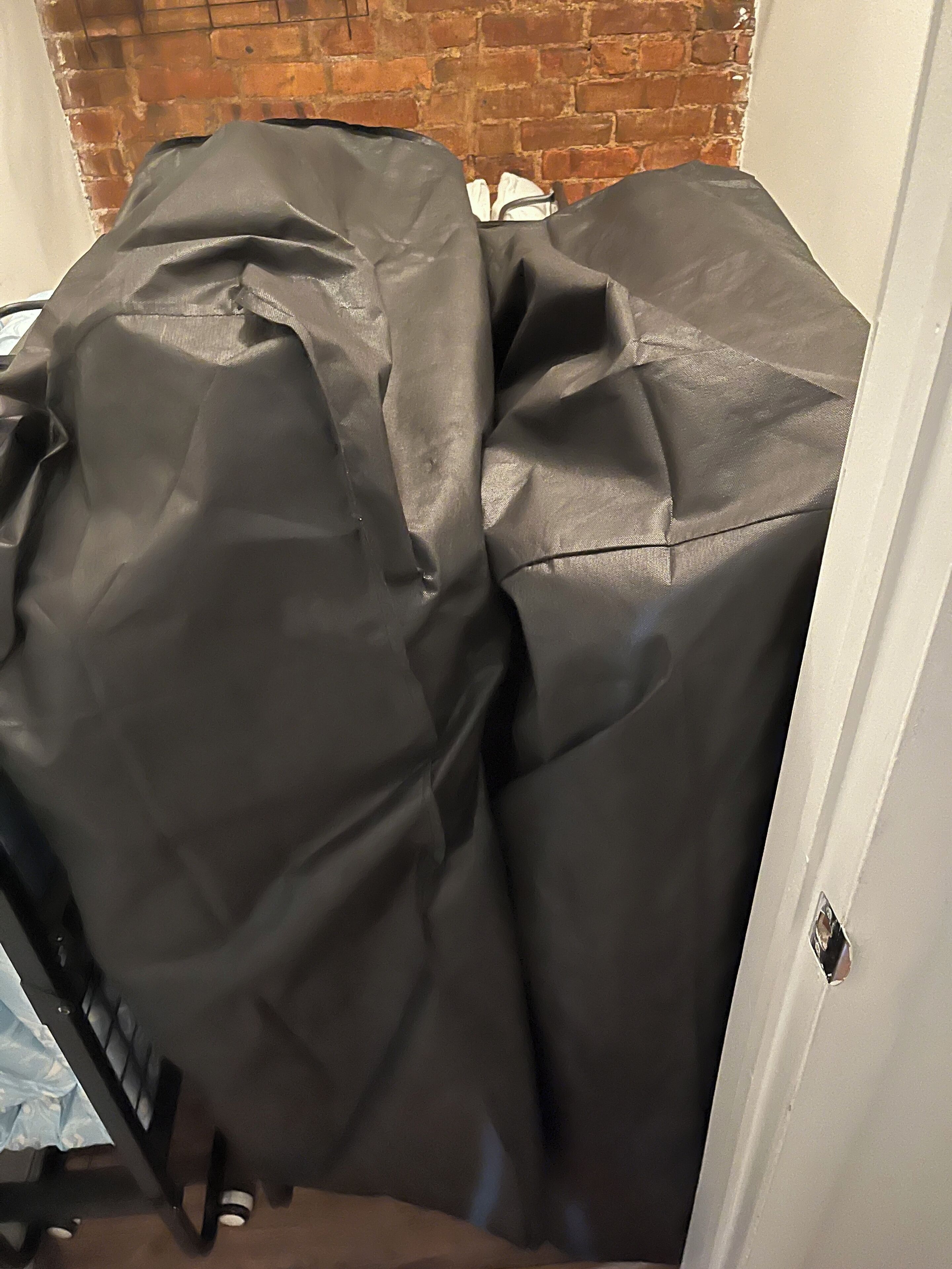 Een kamer met een bakstenen muur en een deels zichtbaar bed met een zwart laken.