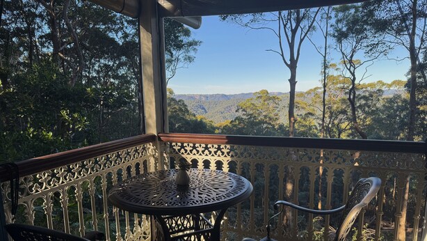 Une terrasse en bois avec une table en métal et deux chaises, donnant sur un paysage boisé.