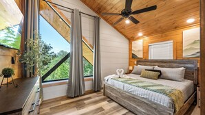 Une chambre avec un plafond en bois, un lit avec une tête de lit en bois, une table de chevet, une fenêtre avec des rideaux et une plante posée sur la commode.