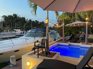 Un área de piscina con sillones de descanso, una piscina pequeña y un barco amarrado cerca.