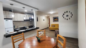 A dining area with a wooden table and chairs, a kitchen with white cabinets, and a yellow sofa in the background. - BEAUTIFUL APARTMENT IN THE BEST SECTOR OF QUITO (Quito)