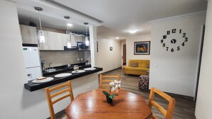 A dining area with a wooden table and chairs, a kitchen with modern appliances, and a living area with a sofa and a clock on the wall. - BEAUTIFUL APARTMENT IN THE BEST SECTOR OF QUITO (Quito)