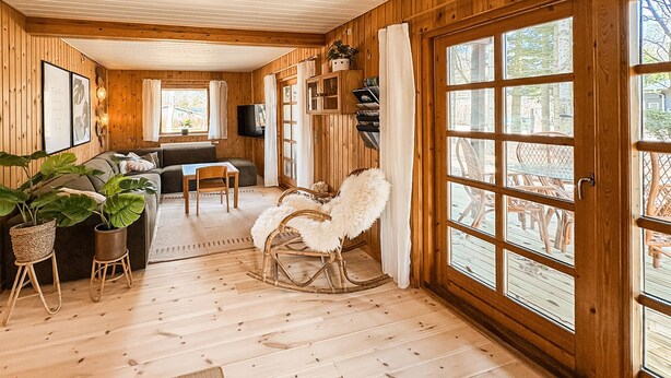 A wooden cabin interior with a sofa, rocking chair, and large windows. - 4 bedroom beautiful home in Thyholm (Thyholm)