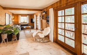 A wooden cabin interior with a sofa, rocking chair, and large windows.
