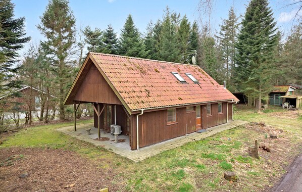 Cozy cabin nestled among tall trees, featuring a porch with a bench and table.