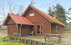 Cozy cabin with a small porch and a bench, surrounded by trees.