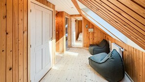 A wooden interior with a sloped ceiling, a hallway leading to a bedroom, and a seating area with cushions. - 4 bedroom beautiful home in Thyholm (Thyholm)