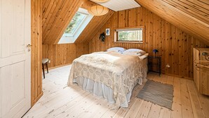 A bedroom with a sloped ceiling, wooden walls, a bed with a white bedspread, a small table, and a window. - 4 bedroom beautiful home in Thyholm (Thyholm)