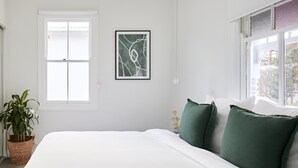 Ein Schlafzimmer mit einem Bett, einer Topfpflanze, einem gerahmten abstrakten Gemälde und einem Fenster mit Blick.