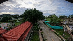 A street view with a red-roofed building, a large tree, and a green construction site. - Petra Hotel (Nuquí)