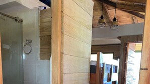 A wooden cabin interior with a shower, toilet, sink, and a wooden bed with towels. - Petra Hotel (Nuquí)