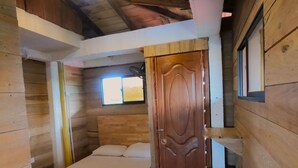 A wooden cabin bedroom with a bed, a window, and a door. - Petra Hotel (Nuquí)