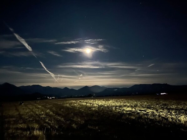 A nighttime landscape with a field, mountains, and a visible moon.