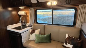 En kompakt autocamper indretning med et tekøkken, et blødt siddeområde og et vindue med udsigt til et sneklædt landskab.