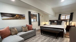 A bedroom with a bed, a sofa, a bench, a painting, and a window.