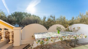 Eine Terrasse im Freien mit einem Tisch, der mit einer floralen Tischdecke bedeckt ist, einem Topfpflanzen und einem Steinboden.