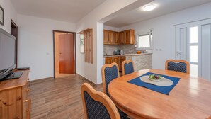Ein Essbereich mit Holztisch und Stühlen, im Hintergrund eine Küche und eine Tür zu einem weiteren Raum.
