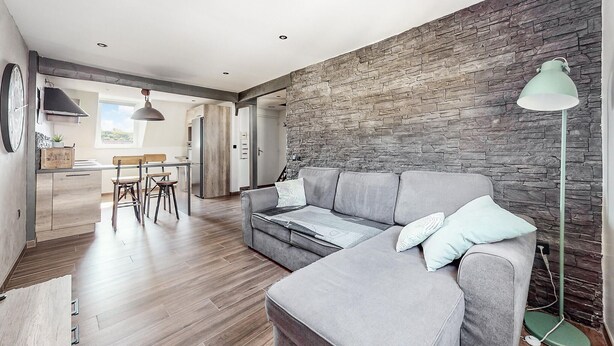 Ein modernes Wohnzimmer mit grauem Sofa, einem Essbereich mit Holzkästen und einer Küche im Hintergrund.