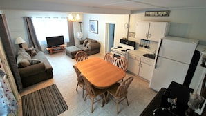 A compact living space with a dining table, chairs, a sofa, a television, a kitchen area with a stove, oven, and refrigerator.
