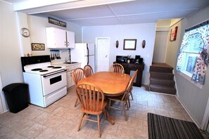 Una cocina compacta con estufa, refrigerador y mesa de comedor con sillas.