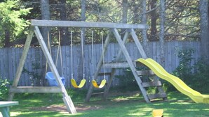 A wooden swing set with two swings and a slide in a backyard.