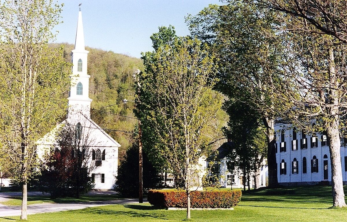 A white church with a steeple, surrounded by trees and a well-maintained lawn.