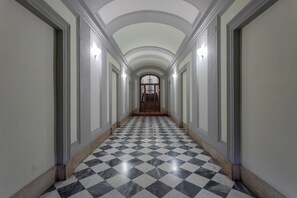 Un couloir doté d’un sol en marbre à carreaux, de murs blancs et d’une porte en bois au fond.
