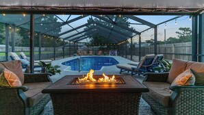 Een terras buiten met een vuurkuil, lounge stoelen en een zwembad.