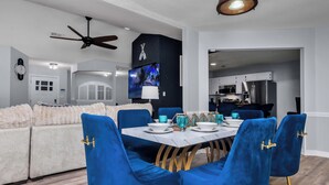 Een moderne woonkamer met een eethoek, met een bank, blauwe fluweelstoelen, een marmeren tafel en een televisie.