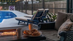 Een zwembadterras met ligbedden, een vuurplaats en een bord croissants.
