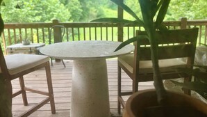 Une terrasse en bois avec une table ronde et deux chaises, entourée de verdure.