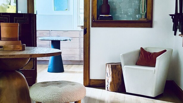 Un salon moderne avec une table à manger en bois, un canapé blanc agrémenté d’un coussin marron et une grande fenêtre donnant sur l’extérieur.