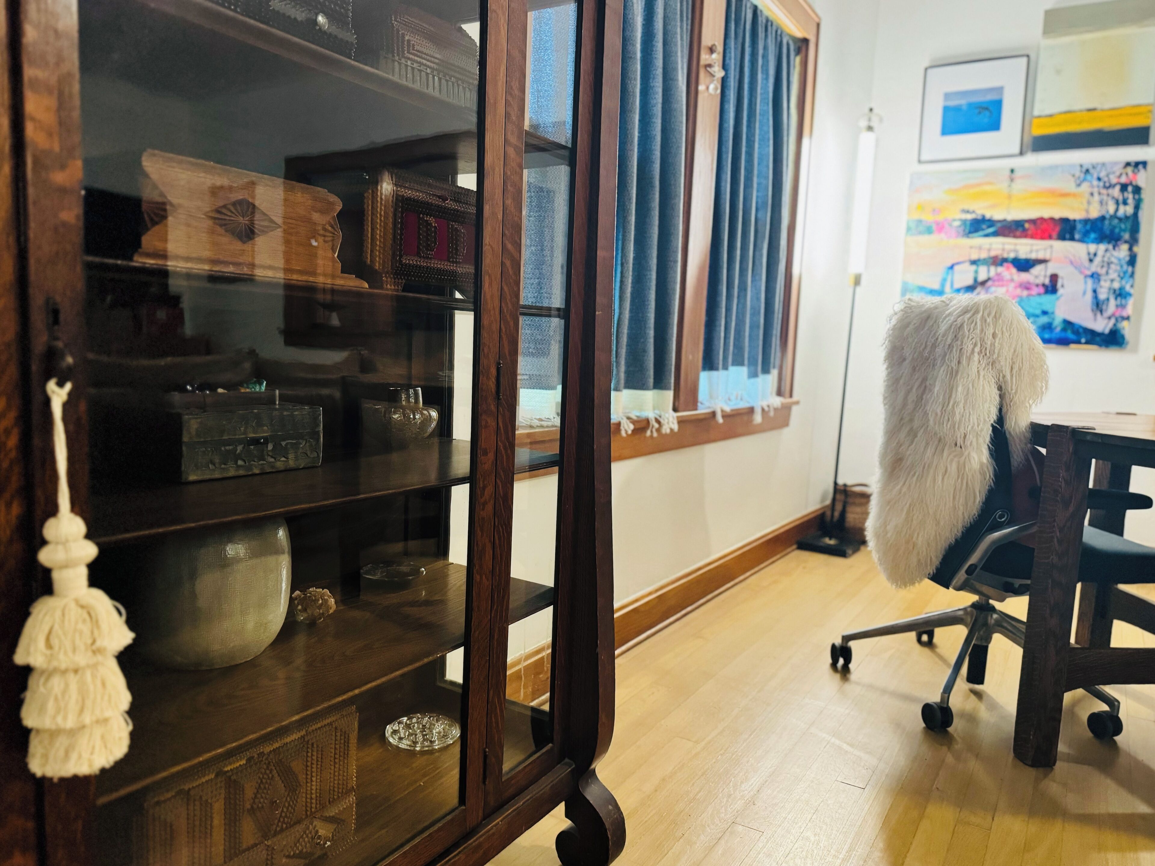 Una habitación con un armario de madera que exhibe varios objetos, un escritorio con una silla y un cuadro en la pared.