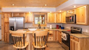 Una cocina con armarios de madera, un refrigerador de acero inoxidable, un lavamanos doble y una mesa de comedor de madera con sillas.