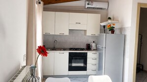 Une cuisine compacte avec des meubles blancs, un four noir et un réfrigérateur blanc. Un vase avec une fleur rouge est posé sur le plan de travail.