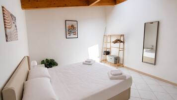 A hotel room with a bed, a wooden headboard, a wall-mounted mirror, a framed picture, and a wooden shelf with a hanging rack.