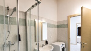 A bathroom with a glass-enclosed shower, a sink, and a washing machine. - BIG Mansard Goldoni [Duomo-M4 Lin Airport] (Milan)