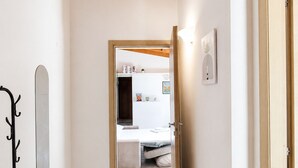 Un couloir avec un plafond en bois, un sol carrelé et une porte donnant sur une chambre à coucher équipée d’un lit et d’une commode.