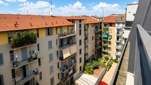 Un immeuble résidentiel à plusieurs étages, doté de balcons et d’antennes paraboliques, se dressant sous un ciel bleu azur.