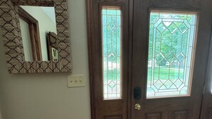 Une porte d’entrée en bois, dotée de panneaux de verre et ornée d’un miroir décoratif sur le mur.
