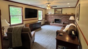 Un salon avec une cheminée, un ventilateur de plafond et un grand téléviseur.