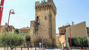 A historic stone tower with a flag on top, situated in a town square with modern buildings around. - House in Provence  (Pertuis)