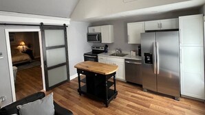 A compact kitchen with modern appliances, a dining table, and a sliding door leading to a bedroom.