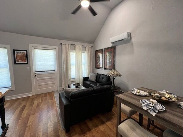 A living room with a black sofa, a dining table with plates, and a ceiling fan.