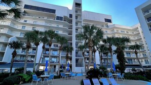 Un hôtel moderne doté de nombreux balcons, d’un espace piscine avec des chaises longues et de palmiers.